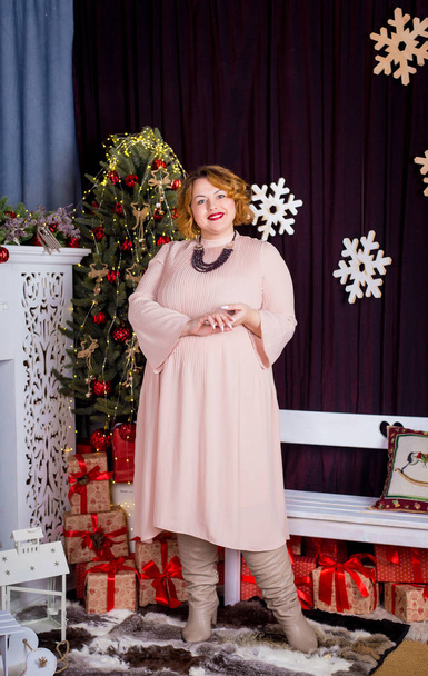 Beautiful girl in a long pink dress close to the fireplace and Christmas fir - Fotoğraf, Görsel