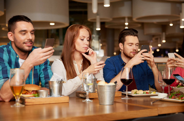 friends with smartphones at restaurant - Fotó, kép