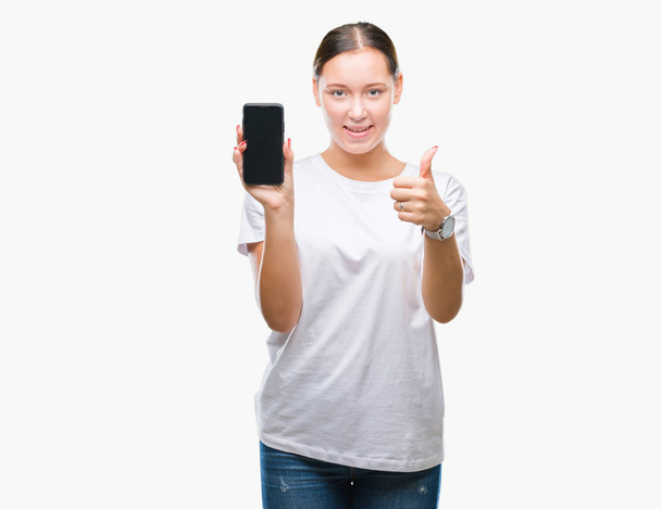 Young beautiful caucasian woman showing smartphone screen over isolated background happy with big smile doing ok sign, thumb up with fingers, excellent sign - Φωτογραφία, εικόνα