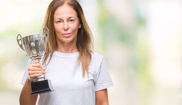 Orta yaş İspanyol kazanan kadın kupa acımak yüz ciddi düşünüyorum üstünde kendine güvenen bir ifade ile izole arka plan üzerinde tutarak Ödülü kutluyor - Fotoğraf, Görsel