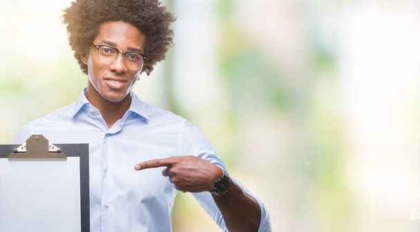 Afro american man holding clipboard over isolated background very happy pointing with hand and finger - Zdjęcie, obraz