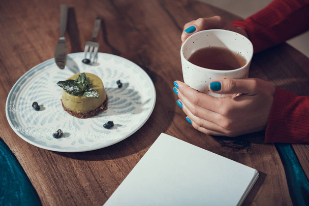 Woman hands holding cup of tea and cake on the plate near - Foto, Imagem