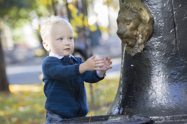 Dziecko myje ręce w fountain. Chłopiec umieścić jego palce pod strumień wody w parku - Zdjęcie, obraz