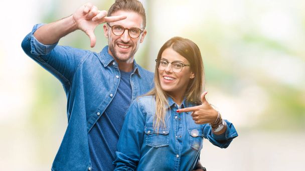 Jovem casal apaixonado vestindo óculos sobre fundo isolado sorrindo fazendo quadro com as mãos e dedos com rosto feliz. Conceito de criatividade e fotografia
. - Foto, Imagem