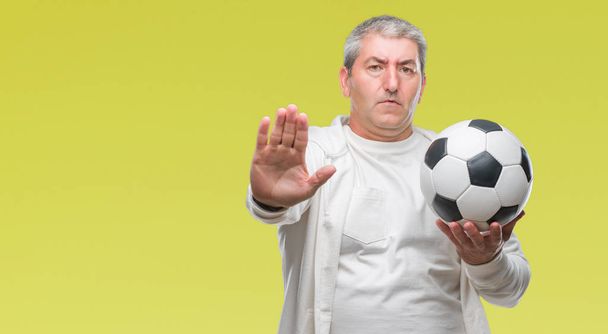 Bello uomo anziano che tiene palla da calcio su sfondo isolato con mano aperta facendo segno di stop con espressione seria e sicura, gesto di difesa
 - Foto, immagini