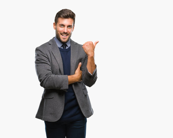 Young handsome business man over isolated background smiling with happy face looking and pointing to the side with thumb up. - Photo, Image
