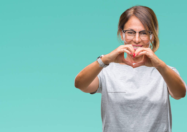 Middelbare leeftijd senior Spaanse vrouw bril over geïsoleerde achtergrond glimlachend in liefde met hartsymbool en vorm met de handen. Romantische concept. - Foto, afbeelding