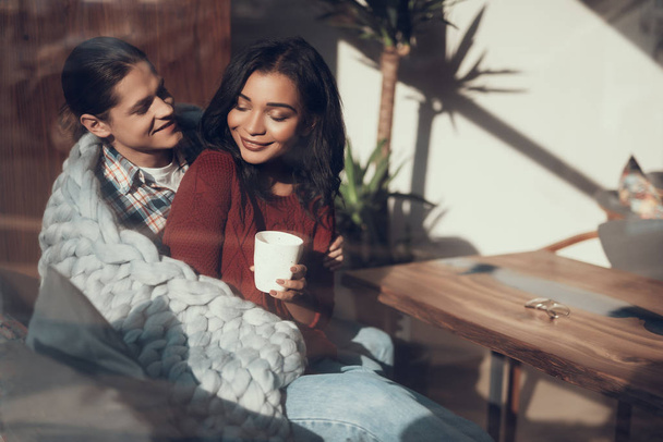 Romantic couple wrapping themselves into warm blanket and smiling - Foto, imagen