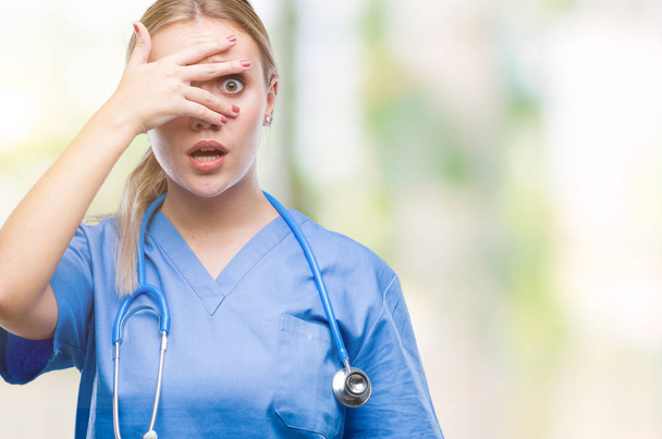 Young blonde surgeon doctor woman over isolated background peeking in shock covering face and eyes with hand, looking through fingers with embarrassed expression. - Фото, зображення