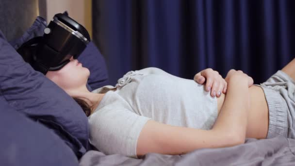 Νεαρή γυναίκα ξαπλωμένη για μαξιλάρια για το κρεβάτι χρήση εικονικής πραγματικότητας, Παρακολουθήστε το βίντεο Vr - Πλάνα, βίντεο
