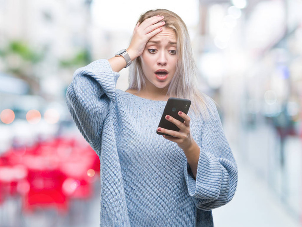 Mladá blond žena SMS odesílání zpráv pomocí smartphone izolované pozadí zdůraznil, s rukou na hlavě, šokoval s hanbou a překvapivou tváří, naštvaný a frustrovaný. Strachu a rozrušení pro chybu. - Fotografie, Obrázek