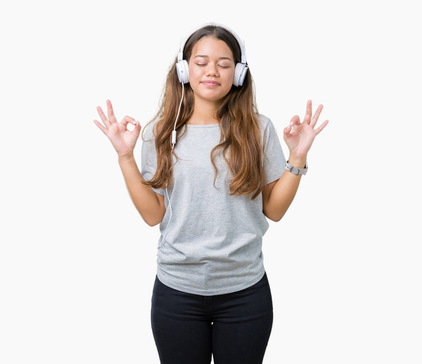 Молода красива жінка в навушниках слухає музику на ізольованому фоні розслабляється і посміхається з закритими очима, роблячи медитаційний жест пальцями. концепція йоги
. - Фото, зображення