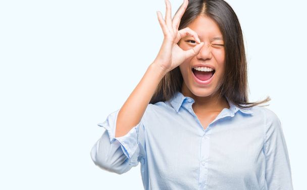 Young asian business woman over isolated background doing ok gesture with hand smiling, eye looking through fingers with happy face. - Foto, Imagen