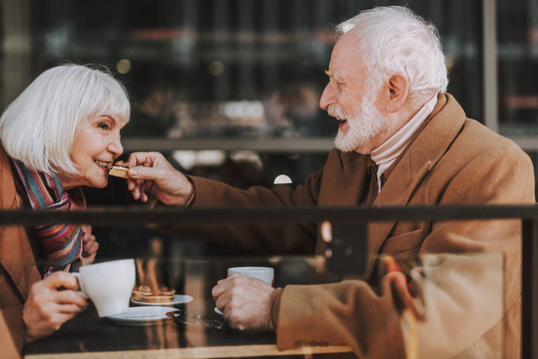 Cheerful old gentleman feeding his wife with delicious cake - Fotoğraf, Görsel