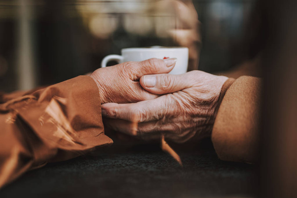 Elderly couple holding hands with hot drink on blurred background - Fotoğraf, Görsel