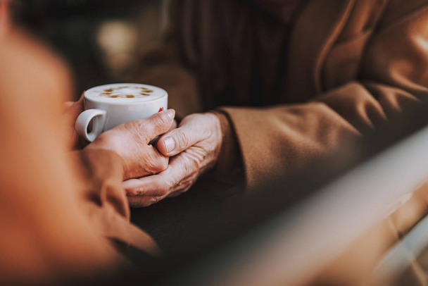 Senior couple holding hands with cappuccino while sitting at the table - 写真・画像