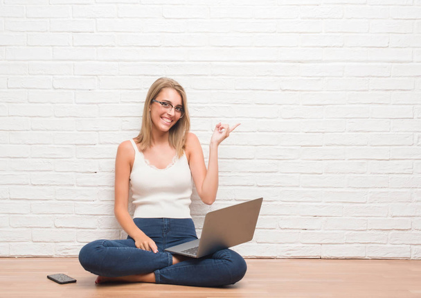 Молодая женщина, сидящая на полу и работающая дома с ноутбуком, очень довольна, показывая рукой и пальцем в сторону
 - Фото, изображение