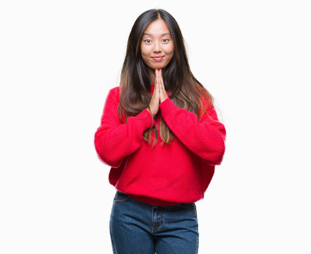 Ellerle birlikte AF emin gülümseyen için soran dua izole arka plan üzerinde kış kazak giyen genç Asyalı kadın. - Fotoğraf, Görsel