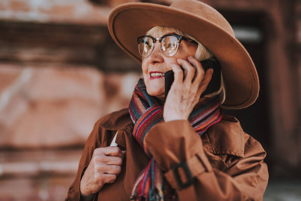 Stylish old woman in hat talking on cellphone on the street - Fotó, kép