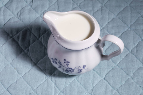 Retro mleczarz z mlekiem na tle niebieski obrus. Krem kawowy - Zdjęcie, obraz