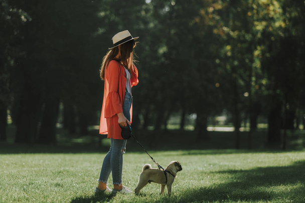 Nuori nainen kävelee koiransa kanssa aurinkoisessa puistossa
 - Valokuva, kuva