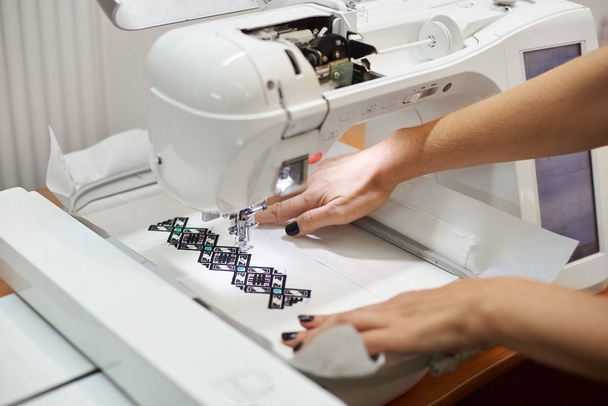 Primer plano de las manos femeninas que trabajan en la máquina de coser y la creación de patrón geométrico colorido en textil blanco
 - Foto, imagen