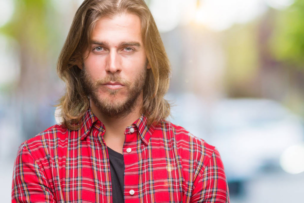 Young handsome man with long hair over isolated background skeptic and nervous, disapproving expression on face with crossed arms. Negative person. - Photo, Image