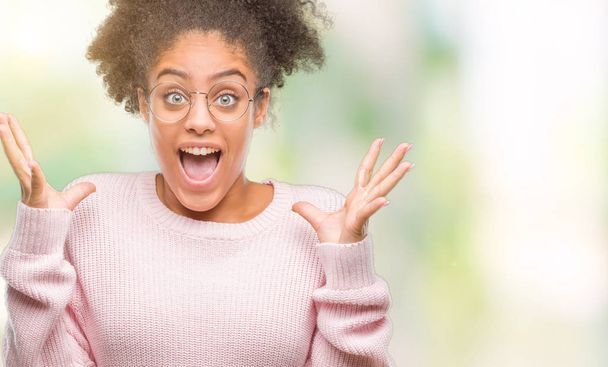 Jeune femme afro-américaine portant des lunettes sur fond isolé célébrant fou et étonné pour le succès avec les bras levés et les yeux ouverts hurlant excité. Concept gagnant
 - Photo, image