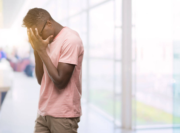 Młody człowiek african american sobie różowy t-shirt z smutny wyrażenie obejmujące twarz rękami podczas płaczu. Koncepcja depresji. - Zdjęcie, obraz