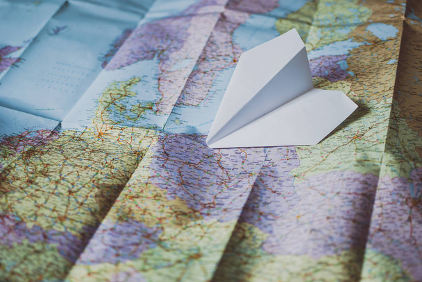 White paper plane laying on the traveler's road map. Vintage retro colors. - Photo, Image