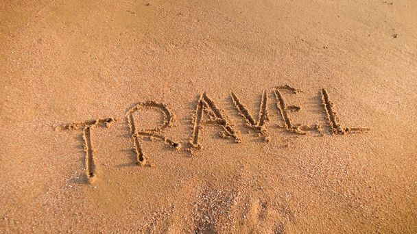 ビーチの砂の上に刻まれた「旅行」という言葉のクローズアップ写真。観光、旅行、旅行、旅の概念. - 写真・画像