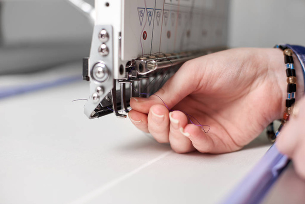 Close up de mãos de mulher de enchimento de fio na máquina de bordado moderno no fundo embaçado brilhante
 - Foto, Imagem