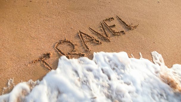 Lähikuva kuva valtameren aallot liikkuvat sana matkustaa kirjoitettu märkää hiekkaa. Käsite matkailu, matkustaminen, matkat ja matkat
. - Valokuva, kuva