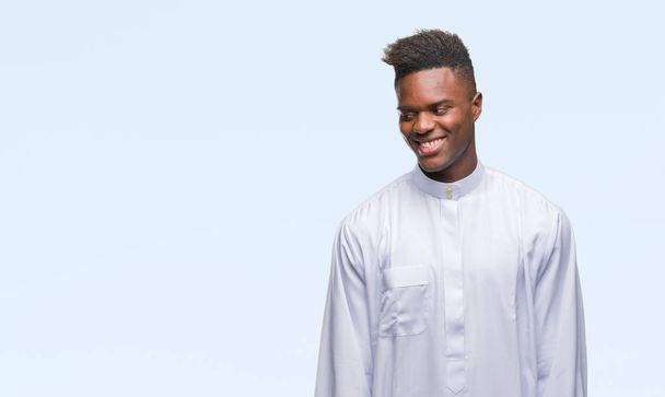 Młody arabski afrykańskiego człowieka noszenia tradycyjnych djellaba na białym tle, patrząc od strony z uśmiechem na twarzy, naturalne wyrażenie. Śmiejąc się pewnie. - Zdjęcie, obraz