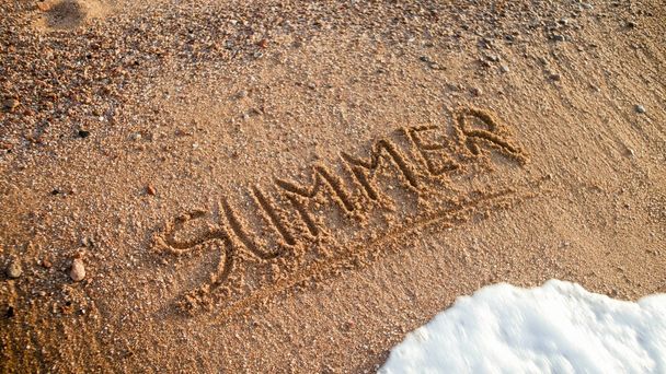 Closeup image of word summer written on wet beach sand. Concept of tourism, traveling, trips and journeys. - Photo, Image