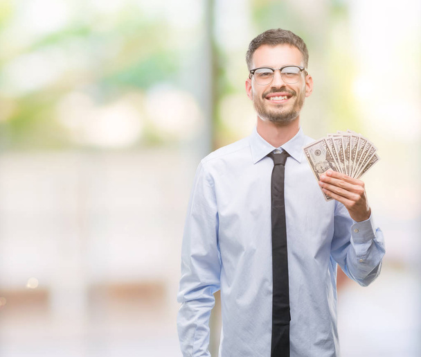Молодой бизнесмен-хипстер держит доллары со счастливым лицом стоя и улыбаясь с уверенной улыбкой, показывая зубы
 - Фото, изображение