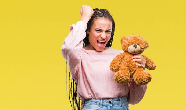 Young african american girl holding teddy bear over isolated background annoyed and frustrated shouting with anger, crazy and yelling with raised hand, anger concept - 写真・画像