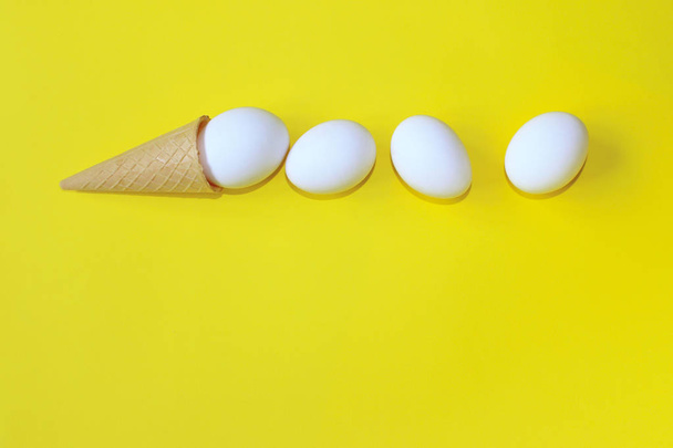 ミニマリズム、食品、ファッションスタイル、イースターのコンセプトです。抽象的な背景。アイス クリーム コーンの白い卵。ミニマル アートなデザイン。黄色の背景の上の白い卵。抽象的なカラフルな食品背景. - 写真・画像