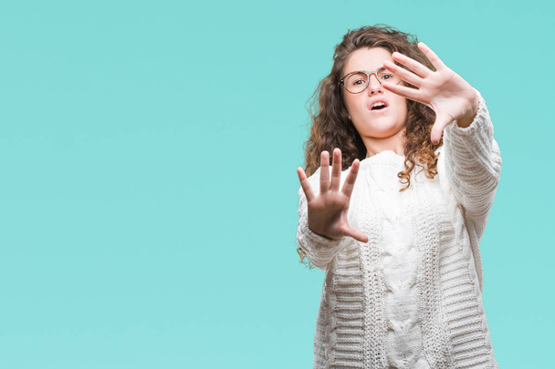 Beautiful brunette curly hair young girl wearing winter sweater over isolated background afraid and terrified with fear expression stop gesture with hands, shouting in shock. Panic concept. - Foto, Imagen