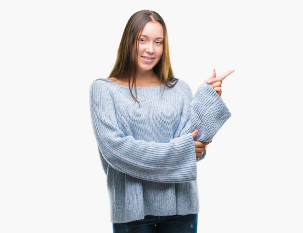 Молода красива біла жінка в зимовому светрі над ізольованим тлом з великою посмішкою на обличчі, спрямована рукою і пальцем в сторону, дивлячись на камеру
. - Фото, зображення