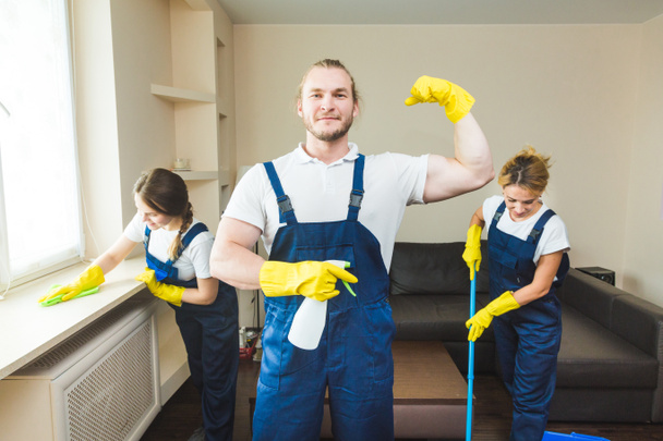 Siivouspalvelu ammattikäyttöön tarkoitetuilla laitteilla työn aikana. ammatillinen keittokomero siivous, sohva kuivapesu, ikkuna ja lattia pesu. mies ja nainen univormussa, haalarit ja kumihanskat - Valokuva, kuva