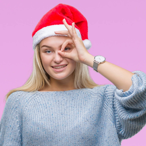 Gülümseyerek el parmakları ile mutlu yüz üzerinden seyir göz ile ok jest yapıyor izole arka plan üzerinde Noel şapka giyen genç beyaz kadın. - Fotoğraf, Görsel