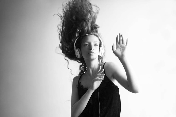 siyah ve beyaz çekim güzel genç kadın beyaz duvar ve dans önünde kulaklık ile müzik dinleme - Fotoğraf, Görsel