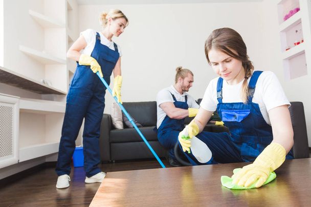Cleaning service with professional equipment during work. professional kitchenette cleaning, sofa dry cleaning, window and floor washing. man and women in uniform, overalls and rubber gloves - Foto, afbeelding
