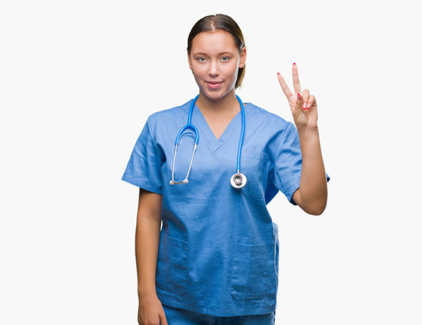 上医療制服を着て若い白人医師女性分離を示す背景と自信を持って、幸せな笑みを浮かべている間 2 つ番号を指で上向き. - 写真・画像