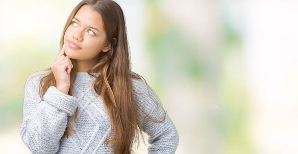 Young beautiful brunette woman wearing sweater over isolated background with hand on chin thinking about question, pensive expression. Smiling with thoughtful face. Doubt concept. - Foto, Bild