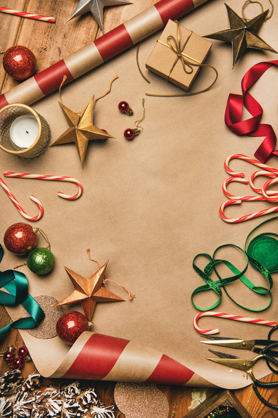 Getting ready for Christmas or New Year holiday. Flat-lay of decorations, ribbons, gift paper, glittering balls, candy canes, top view, copy space, vertical composition. Christmas festive mood - 写真・画像