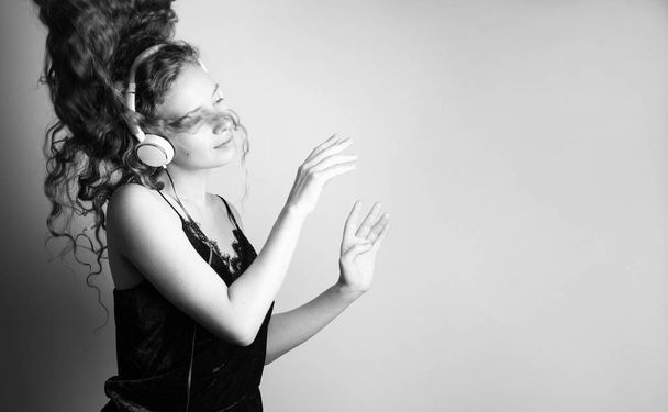 Ασπρόμαυρο πλάνο της όμορφη νεαρή γυναίκα ακούτε μουσική με ακουστικά μπροστά από το λευκό τοίχο και χορό - Φωτογραφία, εικόνα