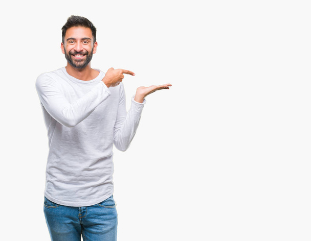Volwassen Spaanse man over geïsoleerde achtergrond verbaasd en lachend naar de camera tijdens het presenteren met hand en met de vinger te wijzen. - Foto, afbeelding