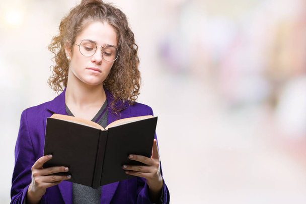 Молодая брюнетка студентка в школьной форме читает книгу на изолированном фоне с уверенным выражением на умном лице, думая серьезно
 - Фото, изображение